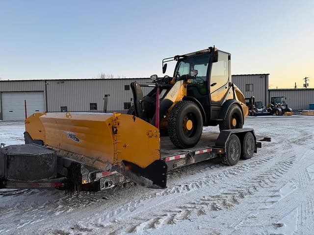 Snow plow mounted on trailer with heavy equipment for winter maintenance in a snowy landscape.