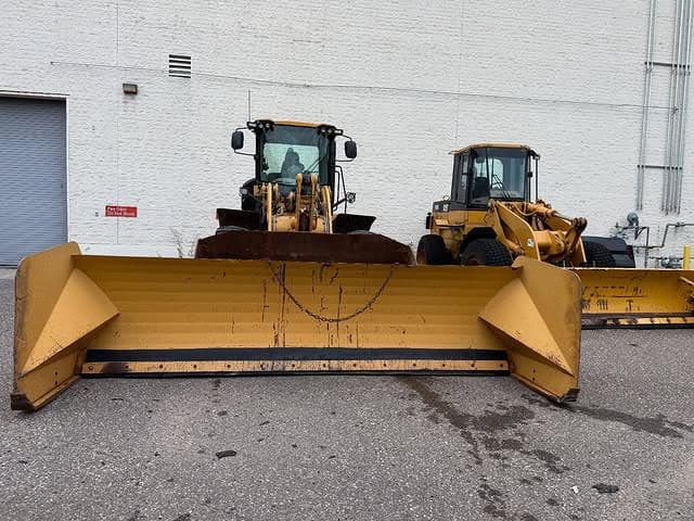 Two yellow construction vehicles with snow plows parked outside a building.