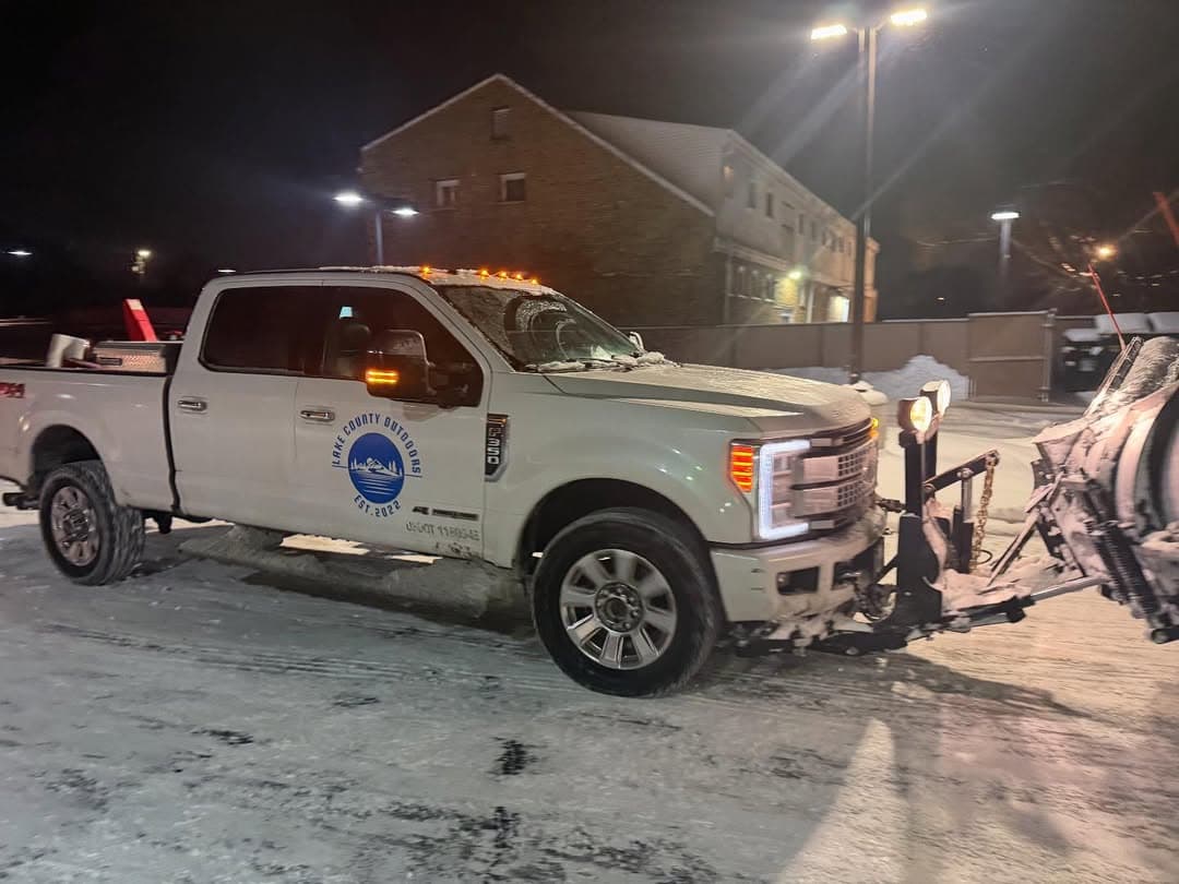 Snow plow truck clearing snow at night in a parking lot, showcasing winter maintenance efforts.