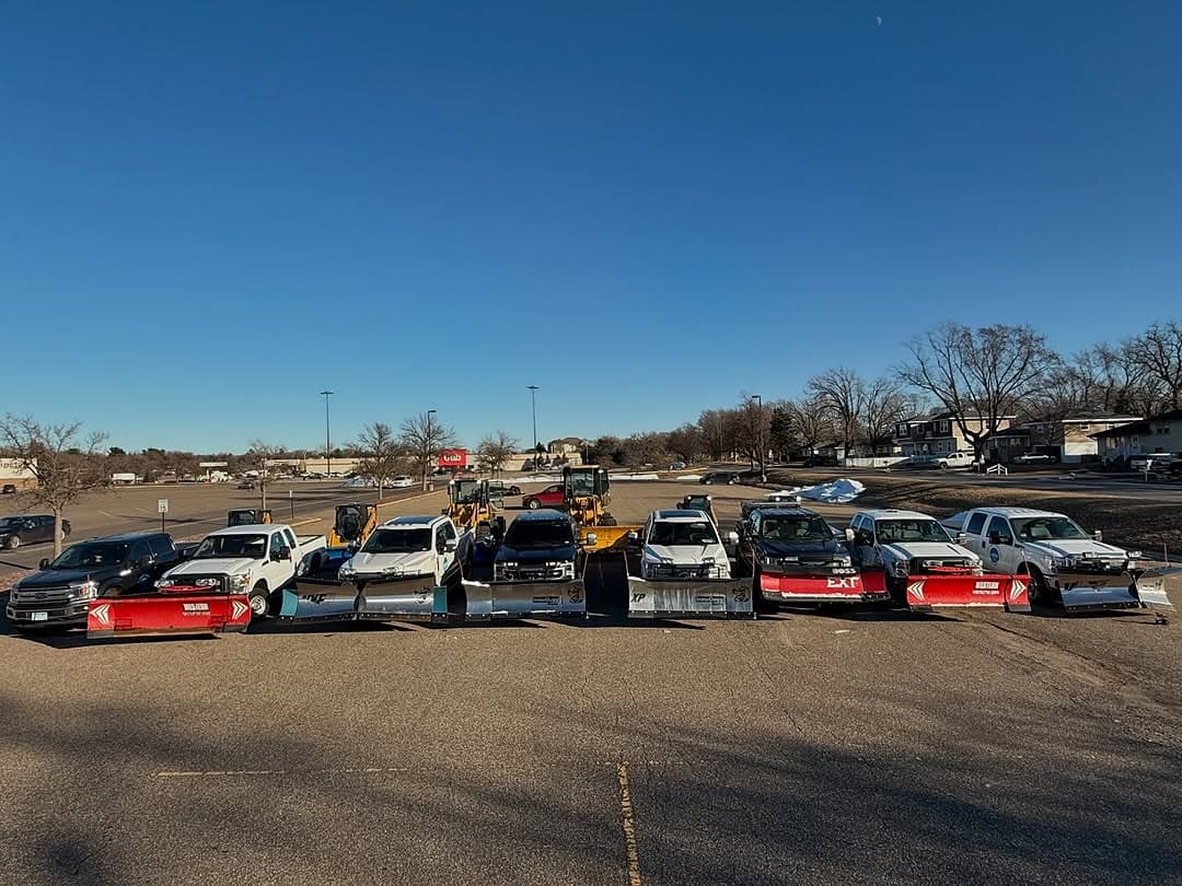 Fleet of snow plows and trucks parked in a lot, ready for winter road maintenance.