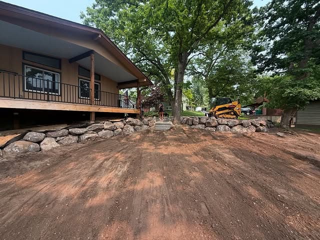 Renovated yard with stone landscaping, porch, and construction equipment nearby.