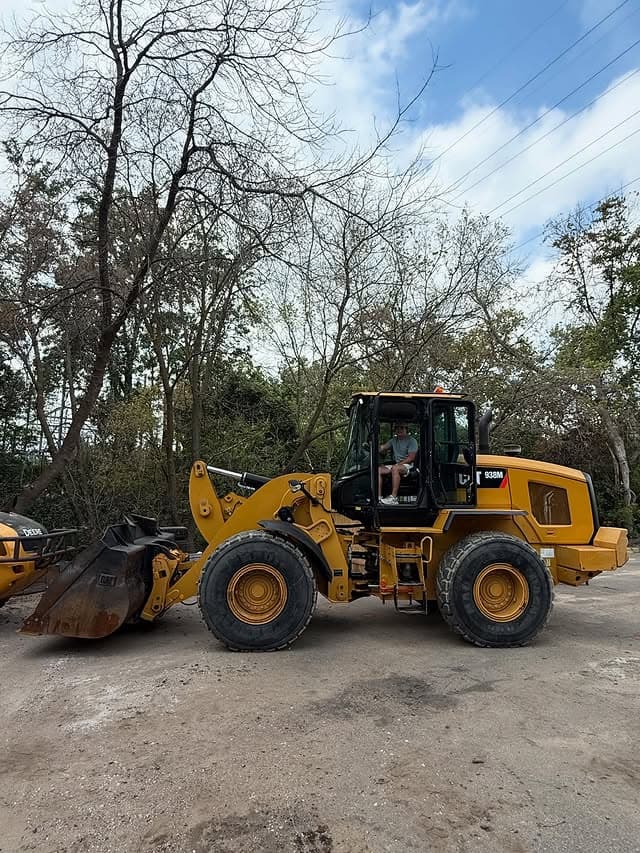 Yellow wheel loader in operation on a construction site surrounded by trees.