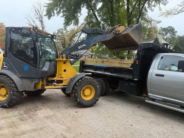 Loader transferring materials from truck at a construction site with trees in the background.